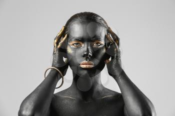 Beautiful woman with black and golden paint on her body against light background�