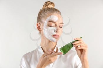Beautiful young woman with facial mask containing aloe vera extract, on light background�
