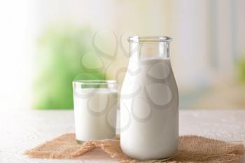 Bottle and glass of tasty milk on light table�