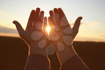 Hands of religious man praying outdoors at sunset�