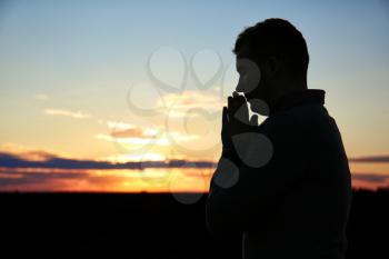 Religious man praying outdoors at sunset�