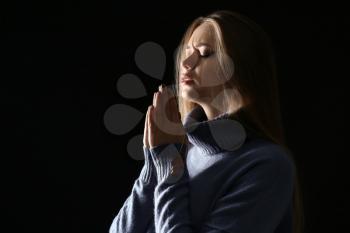 Beautiful young woman praying on dark background�