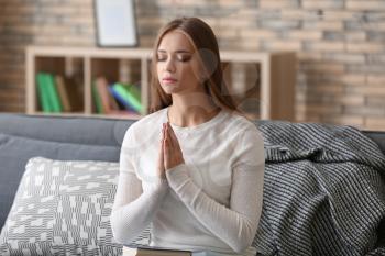 Beautiful young woman praying at home�