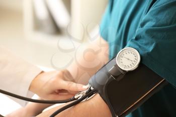 Female doctor measuring blood pressure of male patient in hospital�