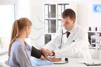 Male doctor measuring blood pressure of female patient in hospital�