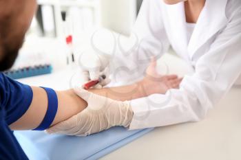 Female doctor drawing a blood sample of male patient in clinic�
