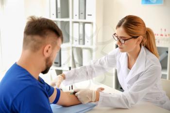 Female doctor drawing a blood sample of male patient in clinic�