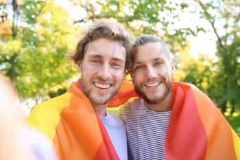 Happy gay couple taking selfie with rainbow LGBT flag in park�