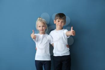 Boy and girl in t-shirts showing thumb-ups gesture on color background�