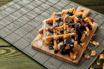 Tasty waffles with chocolate and walnuts on wooden board�