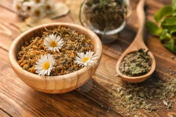 Bowl with dried chamomile flowers on wooden table�
