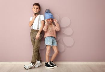 Cute boy and girl in fashionable clothes near color wall�