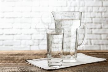 Glass and jug with fresh water on wooden table�