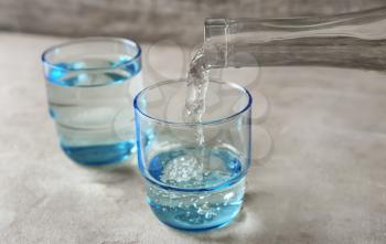 Pouring of fresh water from bottle into glass on table�