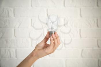 Female hand with eco light bulb on brick background�