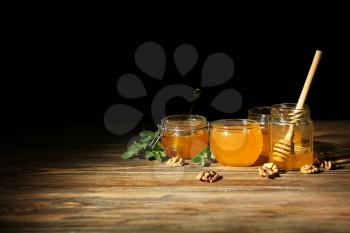 Jars with honey on wooden table against dark background�