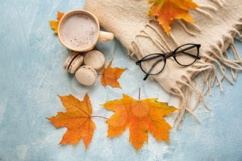 Composition with cup of aromatic coffee, warm plaid and autumn leaves on color background�