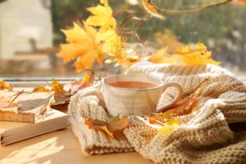 Cup of aromatic tea with warm plaid and autumn leaves on windowsill�