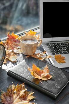 Laptop with coffee, book and autumn leaves on windowsill�