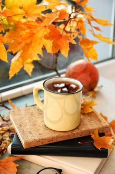 Metal cup of aromatic tea with autumn leaves on windowsill�