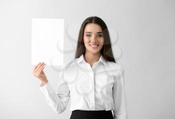 Young businesswoman with blank sheet of paper on light background�