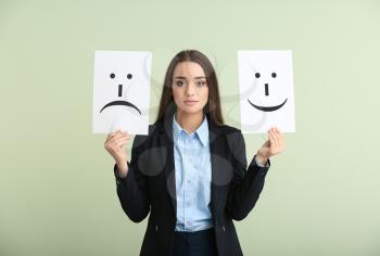 Young woman holding sheets of paper with drawn emoticons on light background�
