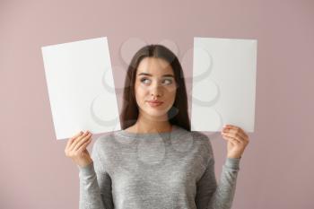 Thoughtful young woman with blank sheets of paper on color background�