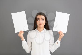 Emotional young woman with blank sheets of paper on grey background�