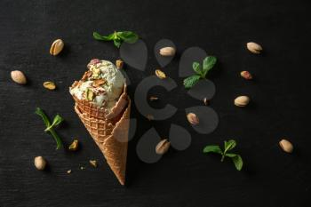 Waffle cone with delicious ice cream and pistachios on dark background�