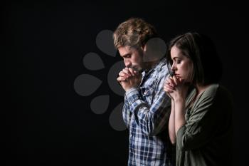 Young praying couple on dark background�