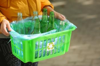 Woman holding box with empty glass bottles outdoors�