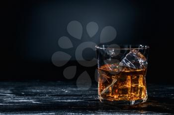 Glass of whisky with ice on wooden table against dark background�