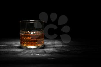 Glass of whisky with ice on wooden table against black background�
