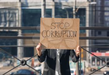 Woman holding placard with text STOP CORRUPTION outdoors�