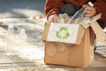 Young woman throwing plastic bottle into cardboard box outdoors. Recycling concept�