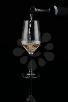 Pouring of white wine from bottle into glass on dark background�