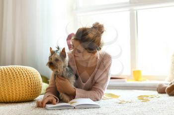 Woman with cute dog reading book at home on autumn day�