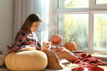 Woman with cute cat resting at home on autumn day�