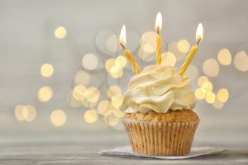 Delicious birthday cupcake with burning candles on grey table  against blurred lights�