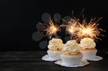 Delicious cupcakes with sparklers on wooden table against dark background�