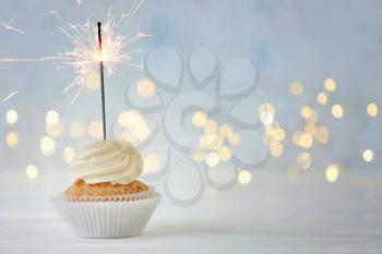 Delicious cupcake with sparkler on white table against blurred lights�