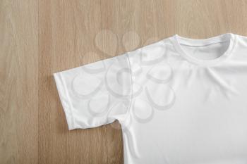 White t-shirt on wooden background, top view�
