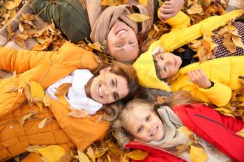 Happy family lying on dry leaves in autumn park�