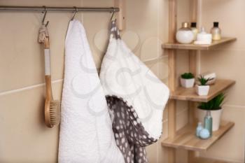 White terry towel, brush and bathrobe hanging on rack in bathroom�