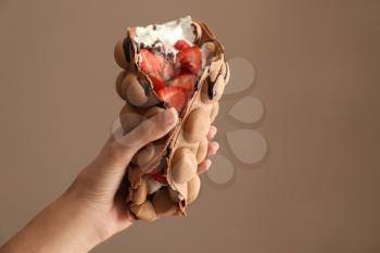 Female hand with delicious sweet bubble waffle on color background�