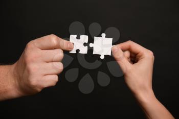 Male and female hands with pieces of puzzle on dark background�