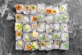 Beautiful flowers frozen in ice cubes on grey background, top view�