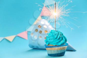 Tasty birthday cupcake with sparkler and party hat on color background�