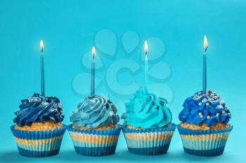 Tasty birthday cupcakes with burning candles on color background�