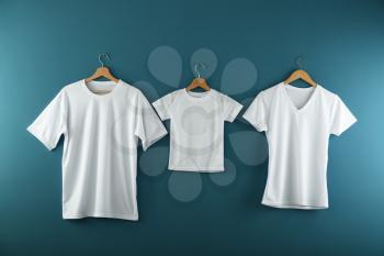 Hangers with blank white t-shirts on color background�